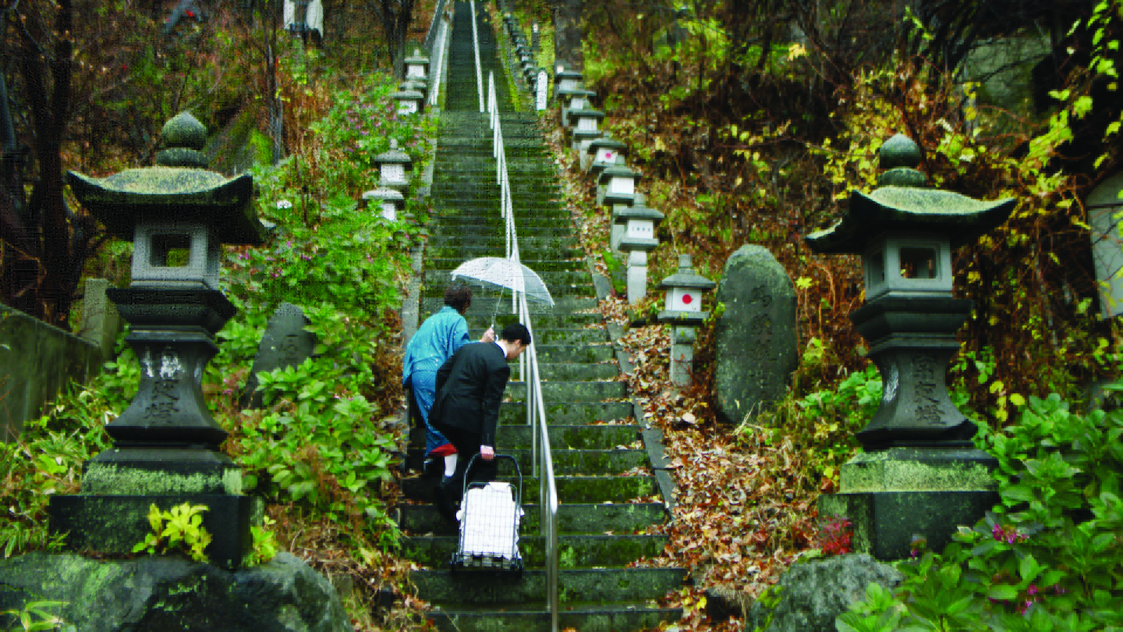 A still from the film, Between Us, of a man and woman walking up steps in rural Japan.