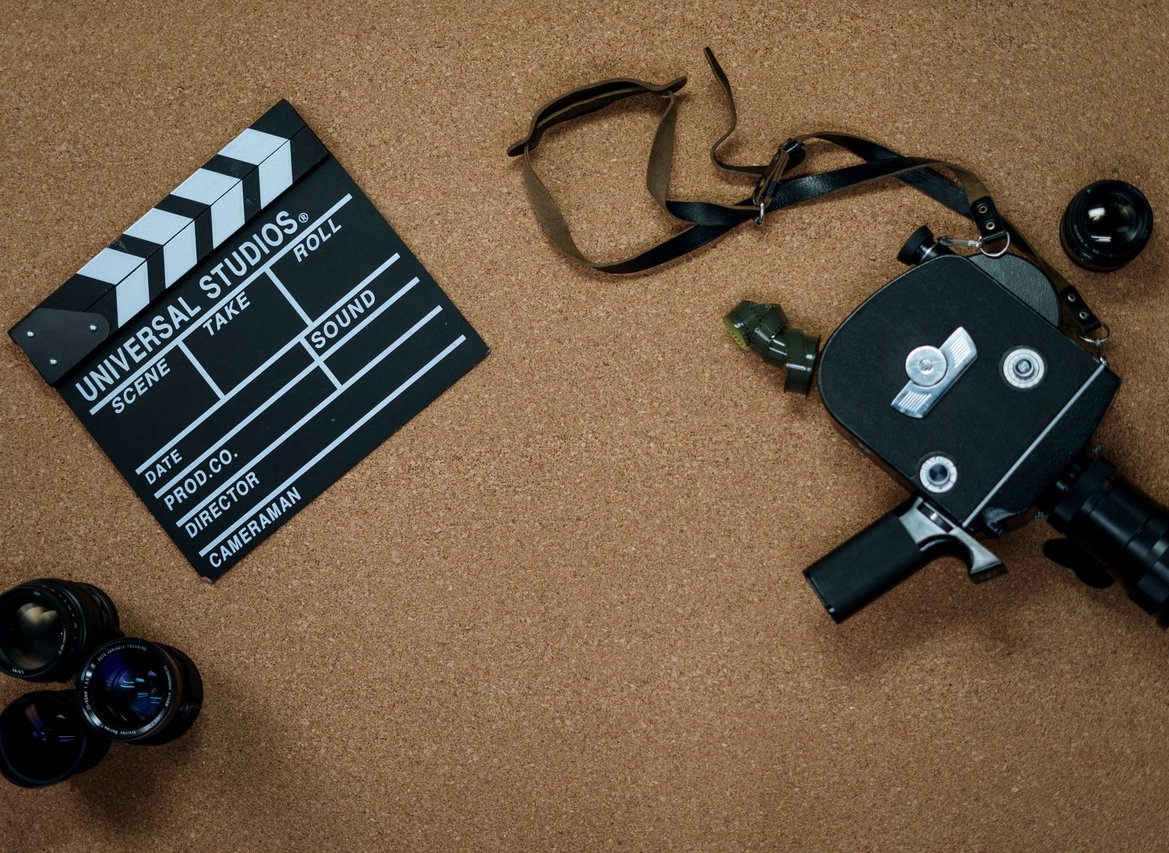 A black and white movie clapboard and an old, black camera.