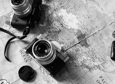 Two cameras rest on top of a world map. The photo is in black and white.