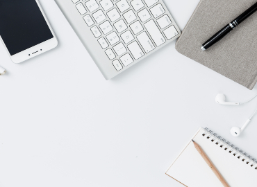 A wireless keyboard, phone, notebooks, pens and a pair of earphones on a white desk.